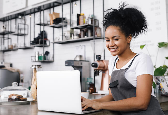 woman at a small shop with apron writing on computer