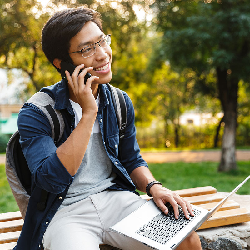 A man sitting on a bench, using a laptop and listening to on-hold messaging