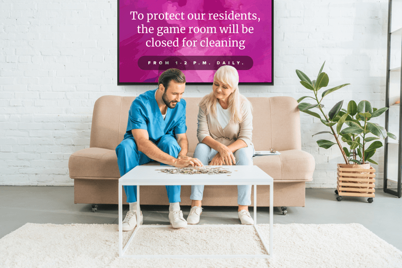 Nurse and senior citizen in a retirement community game room in front of a digital sign