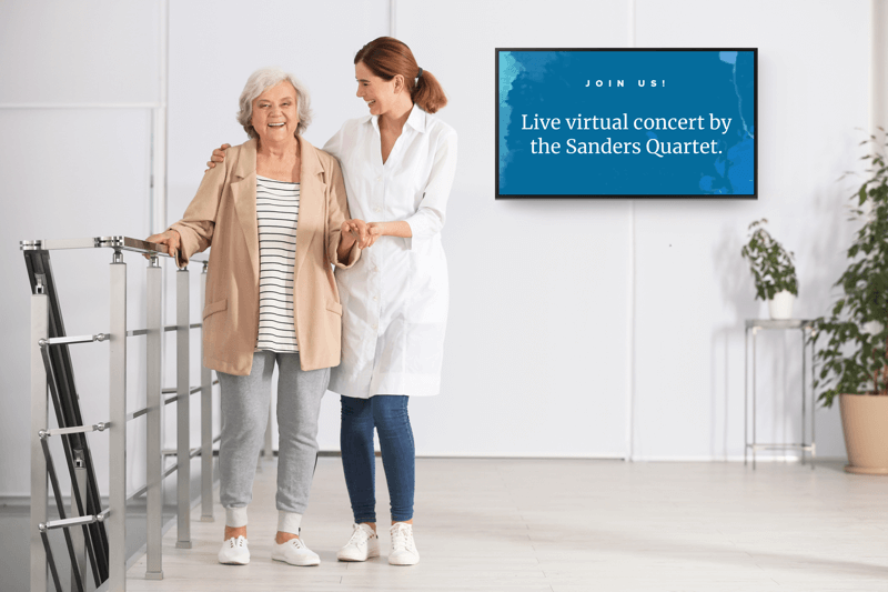 nurse helping an elderly woman, a digital display hangs on the wall